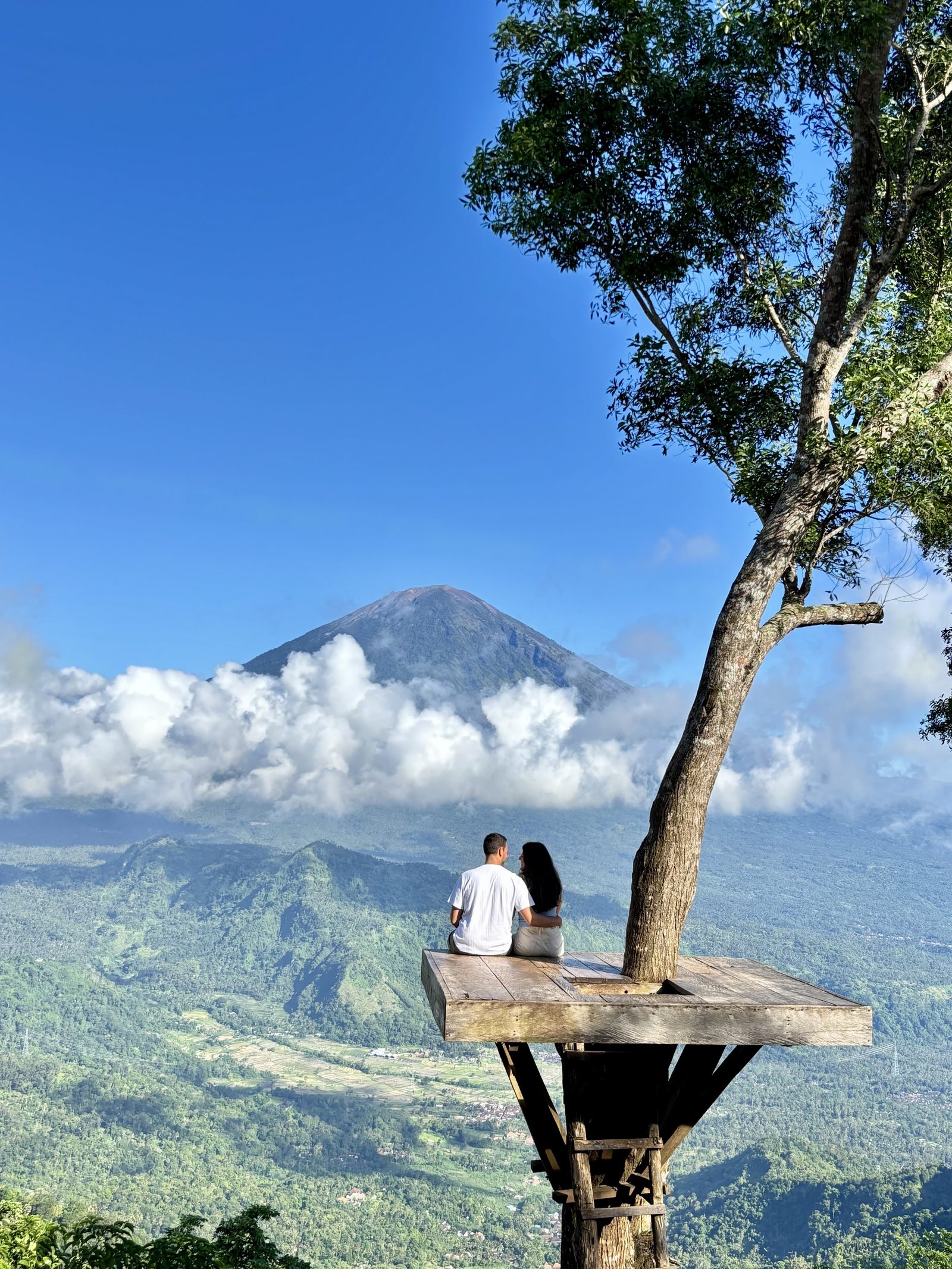 Pareja sentada en plataforma de madera con el volcán Agung y valles de Bali de fondo