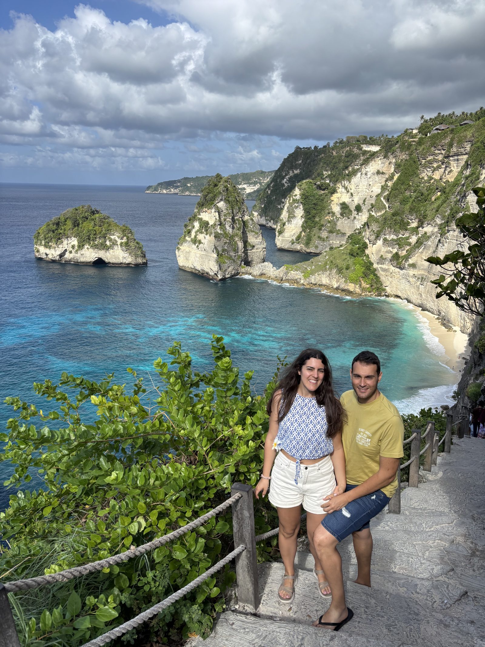 Pareja en las escaleras de Diamond Beach con acantilados y mar turquesa, Nusa Penida
