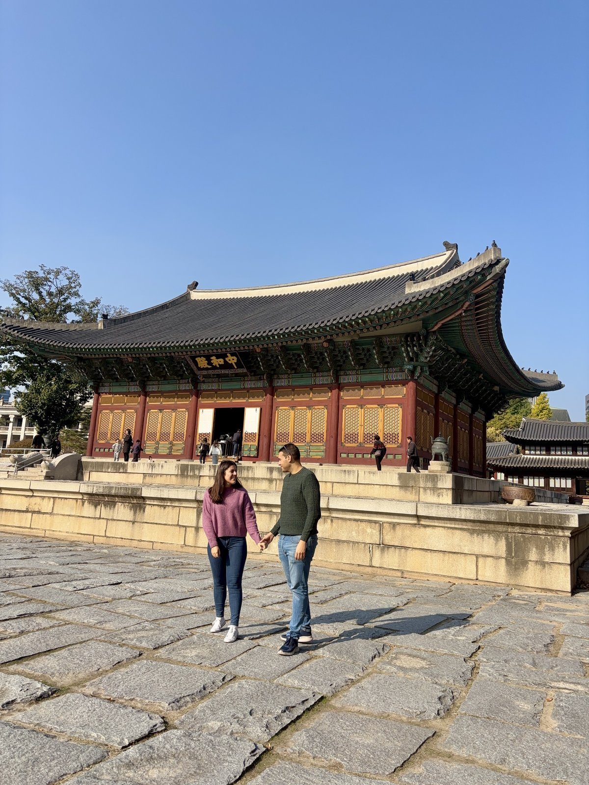 Pareja posando frente al Palacio Deoksugung con tejados tradicionales coreanos al fondo