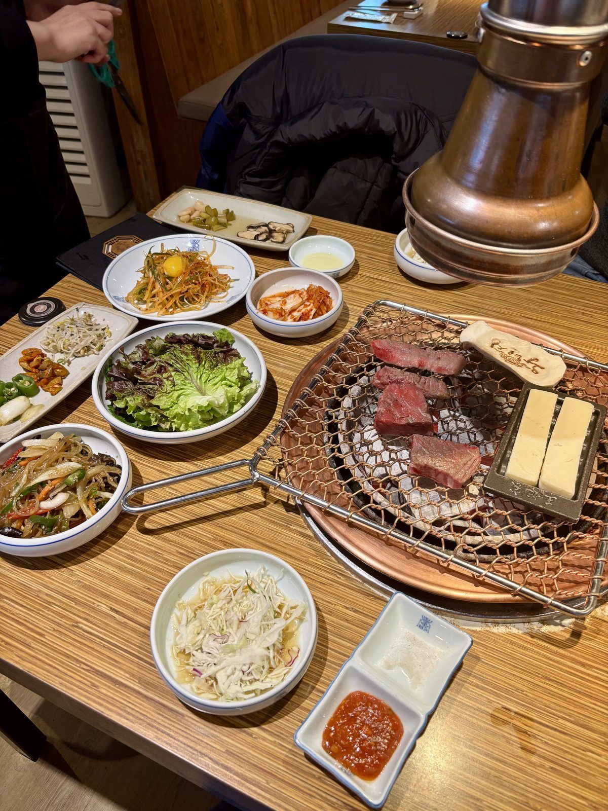 Barbacoa coreana gogigui con carne asándose en la parrilla y platos banchan en la mesa