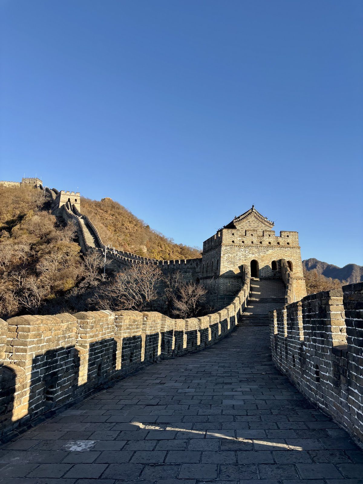 Camino sobre la Gran Muralla China en Mutianyu con una torre de vigilancia al fondo y cielo azul