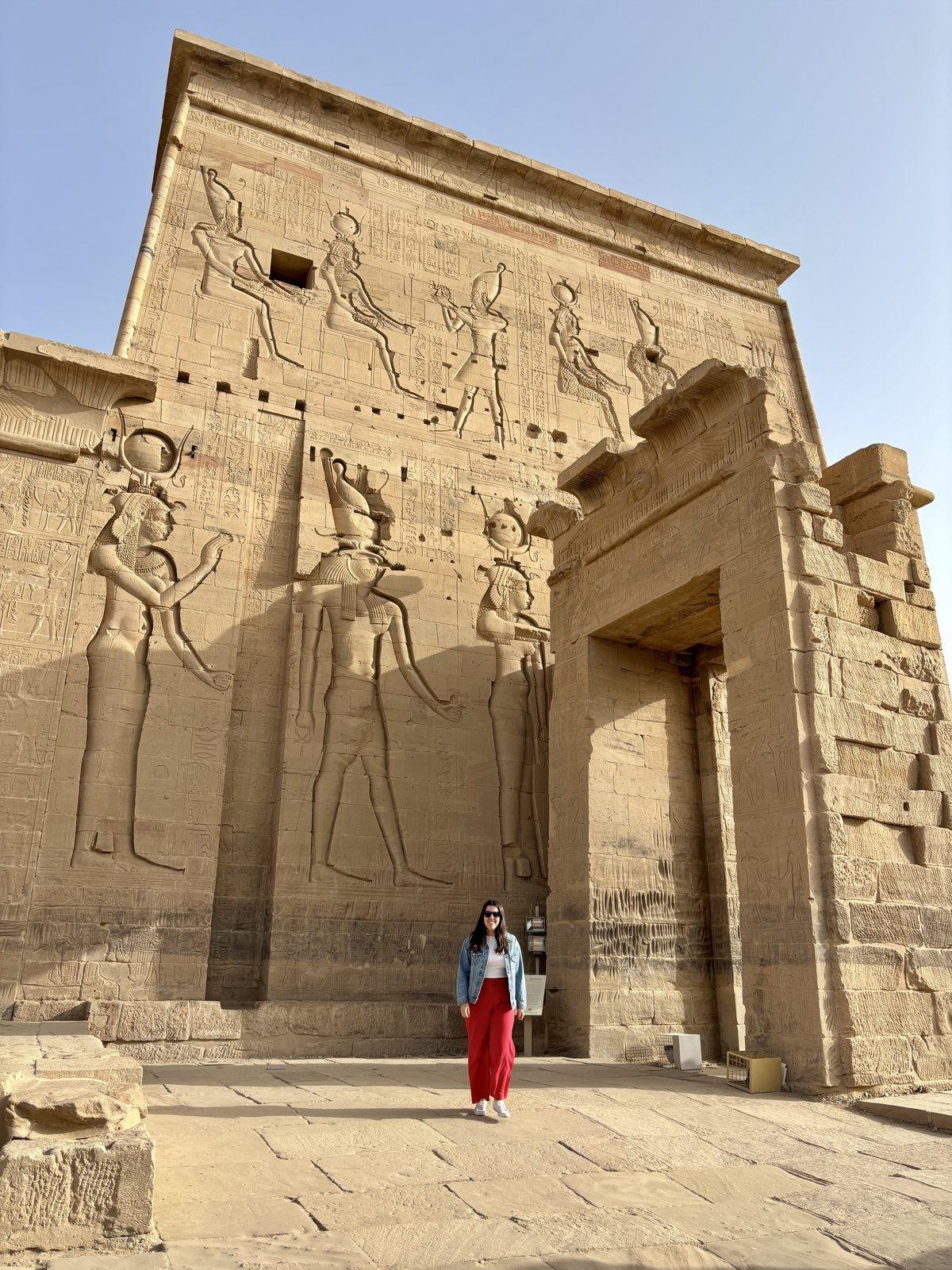 Moni ante la fachada del Templo de Isis en la isla de Filae, Asuán, con relieves de dioses egipcios