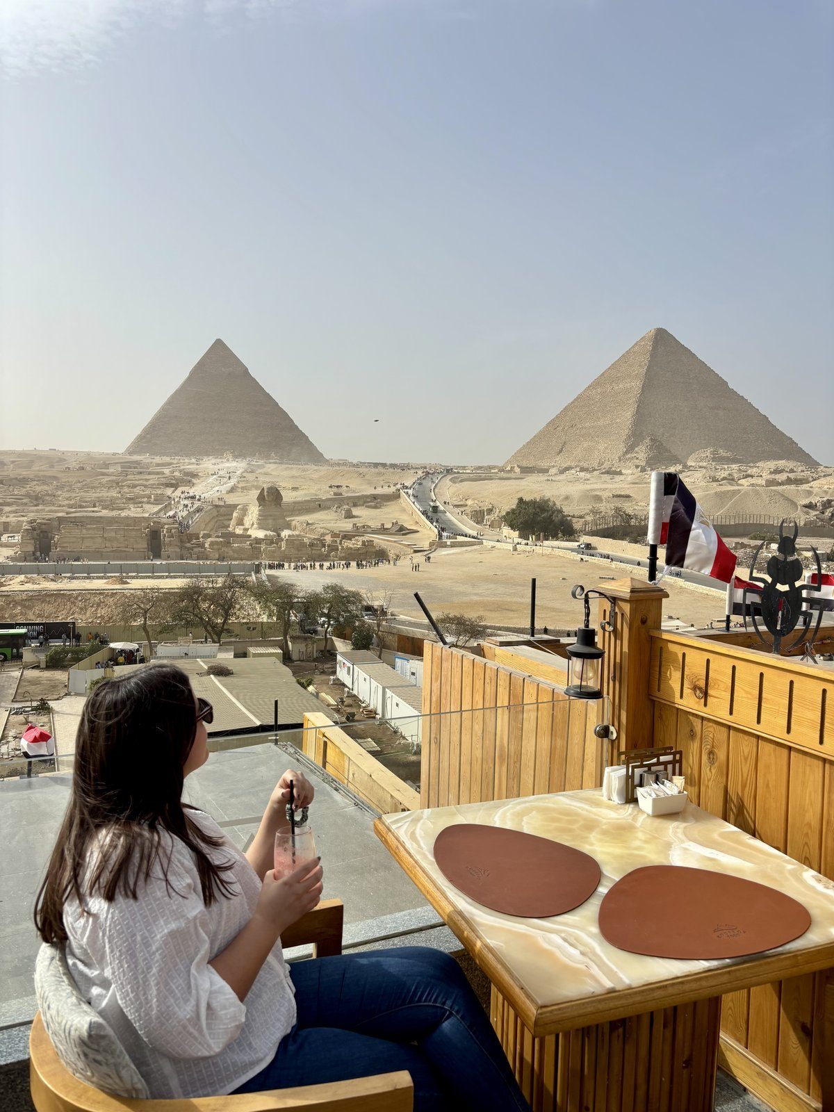 Moni tomando un cóctel en una terraza con vista panorámica a la Esfinge y las Pirámides de Guiza