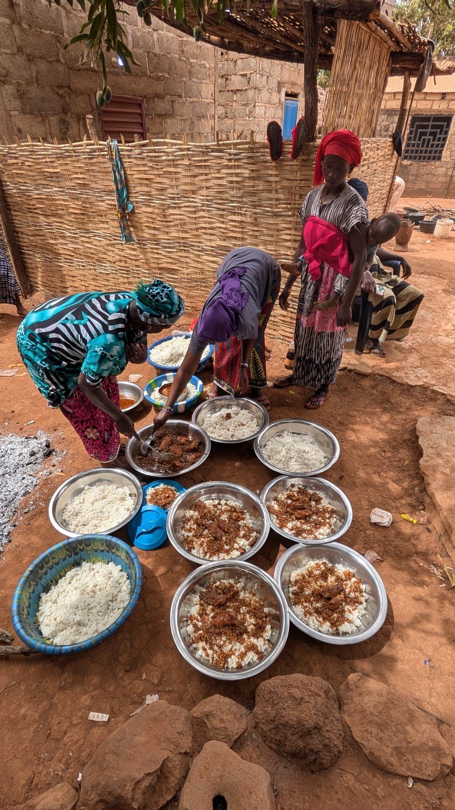 Mujeres del pueblo cocinando thieboudienne en cuencos tradicionales, País Bassari, Senegal