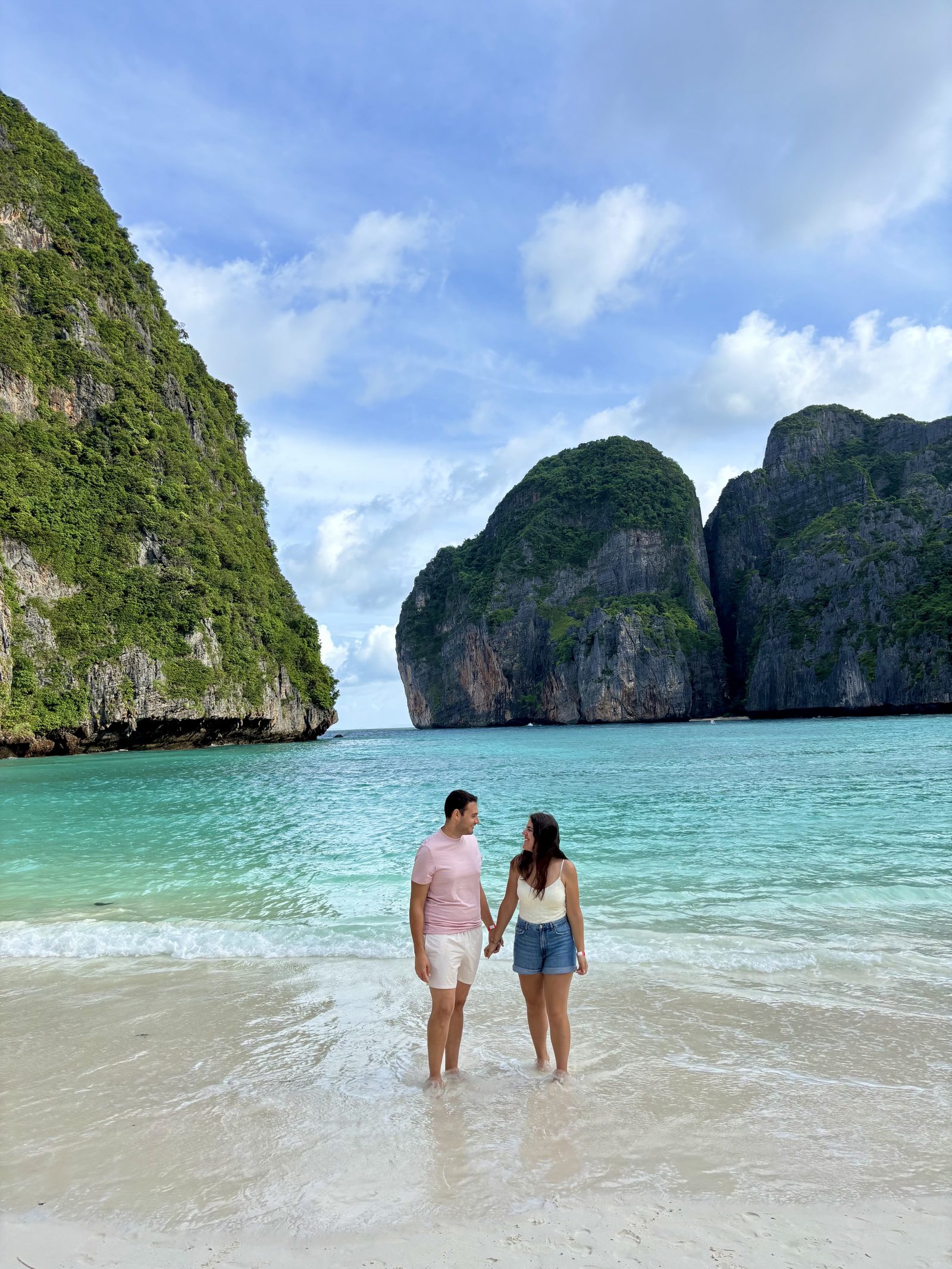 Pareja de la mano en Maya Bay con los acantilados de Koh Phi Phi al fondo